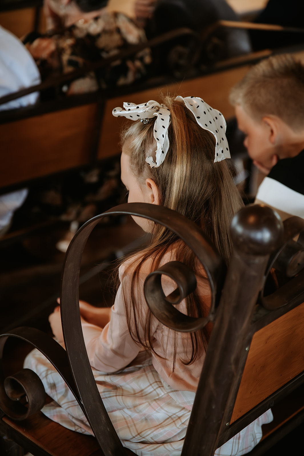 This image shows wedding guests attentively watching the couple at the altar during their ceremony. The moment reflects a shared emotional experience as friends and family witness the couple’s vows and celebration of love.